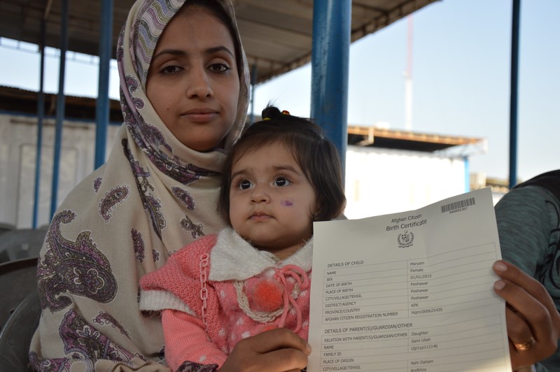Afghan woman holding her daughter and a copy of her birth certificate.