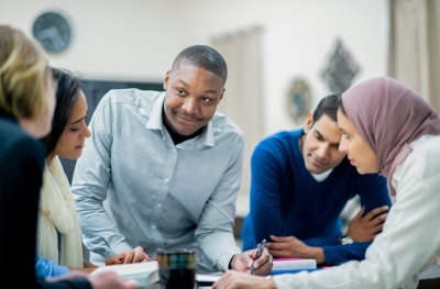 A young Black man leads a group discussion with his multi-ethnic colleagues.